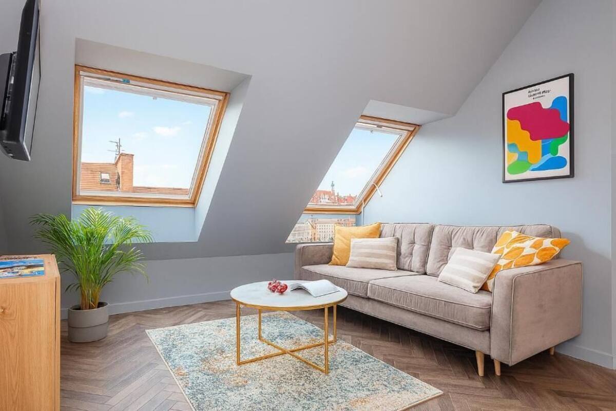 En modern lägenhet i loftstil med högt i tak, två takfönster, en beige soffa, ett litet runt bord och en krukväxt.