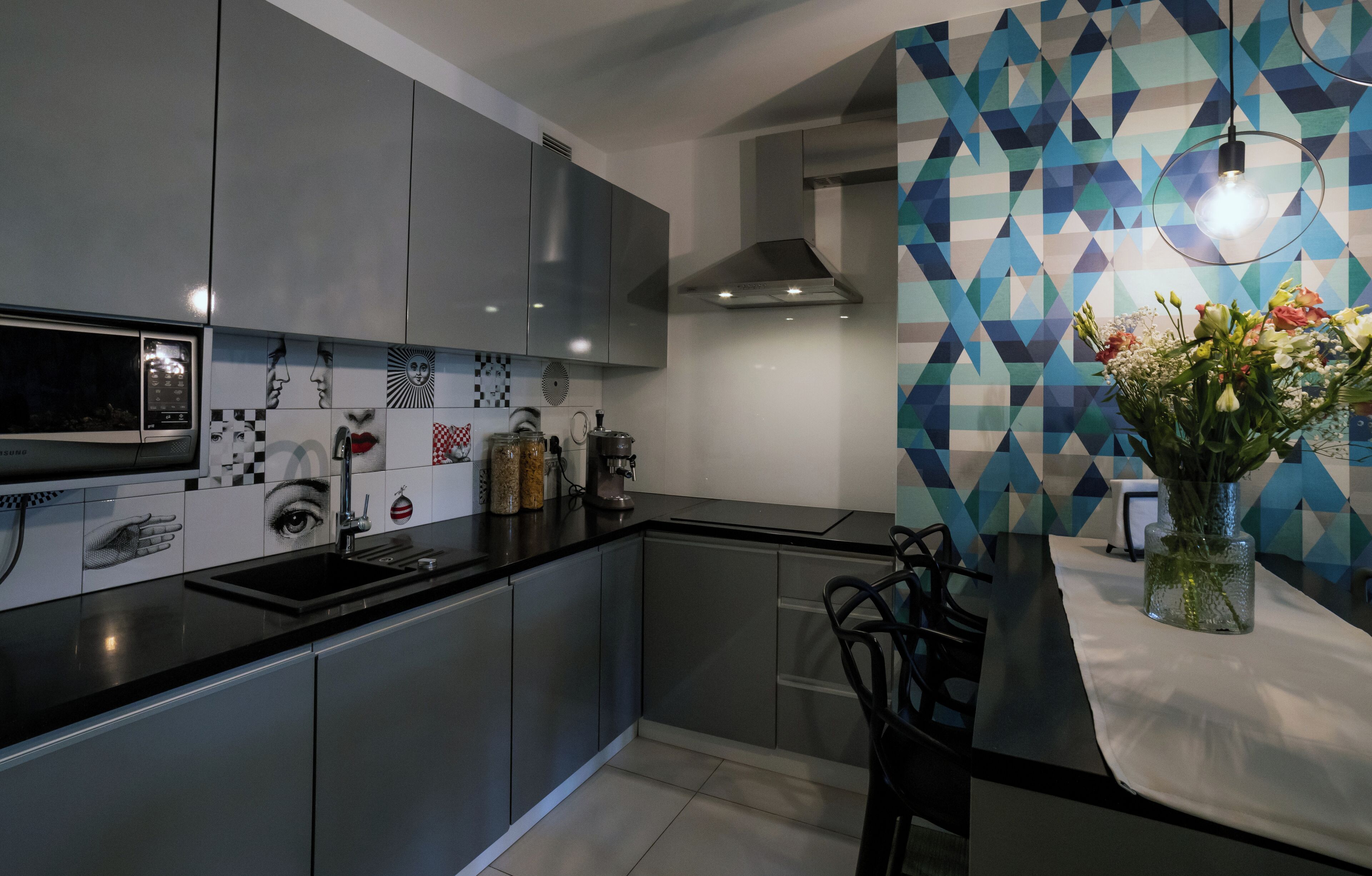 A modern kitchen with grey cabinets, a black countertop, and a geometric patterned backsplash.