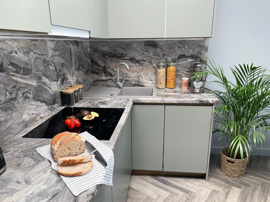 Una cocina moderna con salpicadero de mármol, un lavamanos empotrado y una pequeña isla con tabla de cortar y pan. Hay frascos en la encimera y una planta en maceta en la esquina.