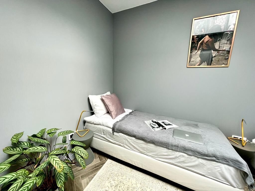 A small, neatly arranged bedroom with a single bed, a bedside table, a lamp, and a framed picture on the wall.