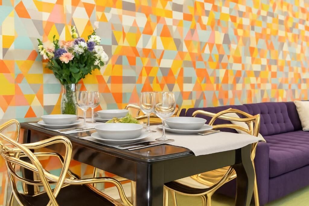 A dining area with a black table set for four, gold chairs, and a purple sofa in the background.