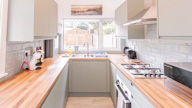 A modern kitchen with light grey cabinets, a wooden countertop, a gas stove, and a window providing a view of the outside. - Pass the Keys | Comfortable Flat with Patio | Sleeps 4 (Westcliff-on-Sea)