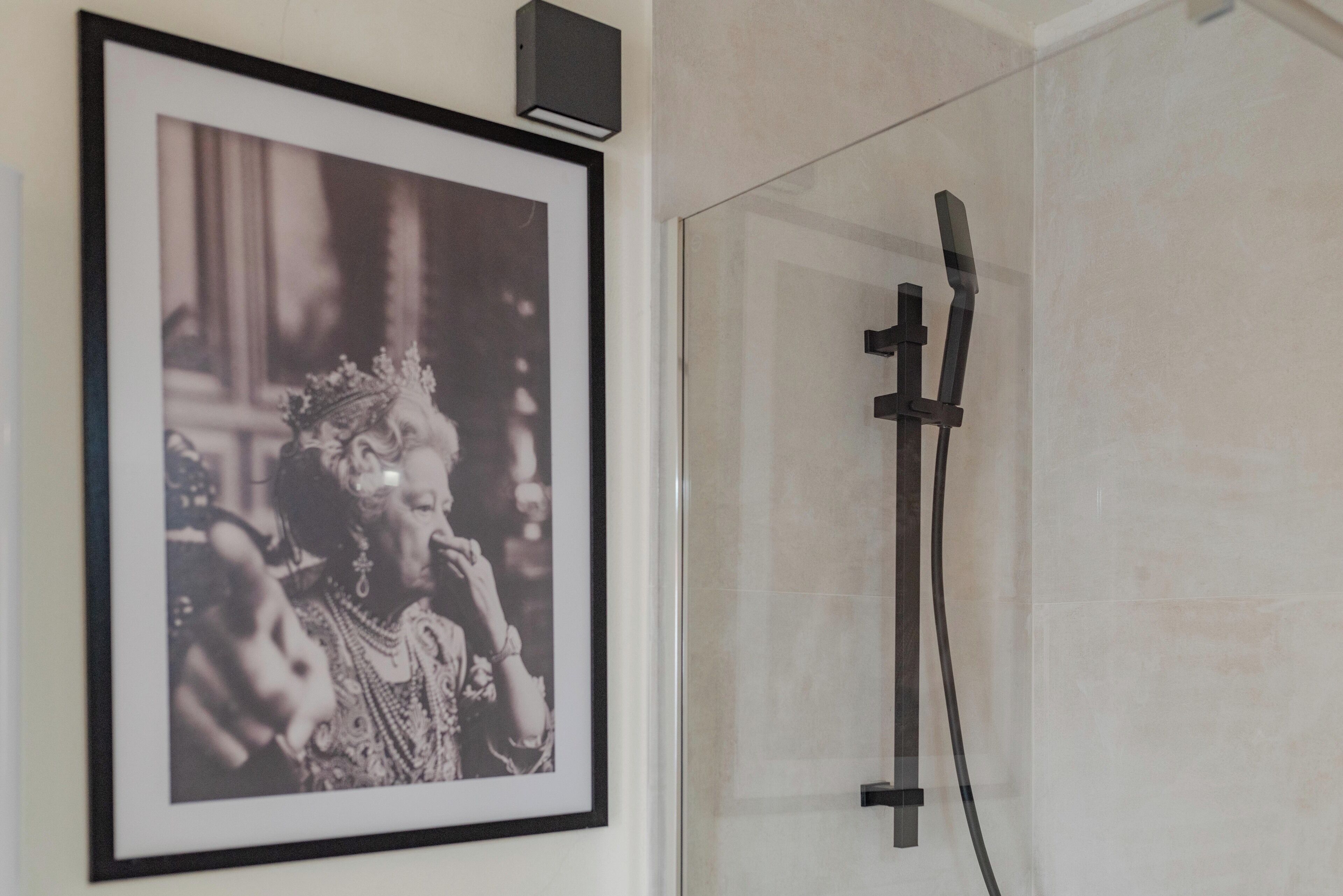 A framed photograph on the wall, a showerhead, and a tiled wall.