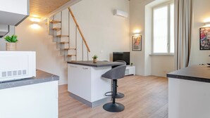 A modern kitchen with a built-in island, a staircase, and a large window with curtains. - Torino essential Loft (Torino)