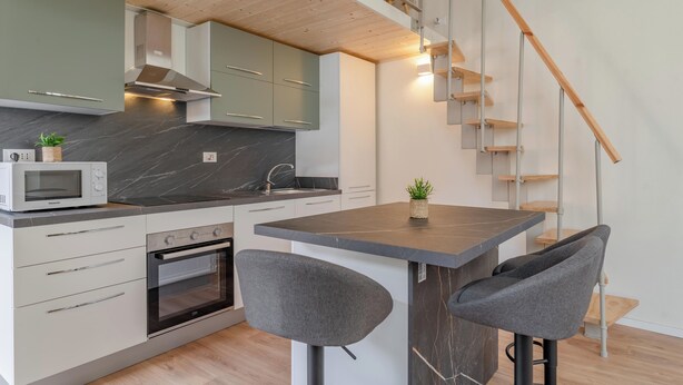 A modern kitchen with a central island, built-in oven, and a microwave. There is a staircase with wooden steps and a railing. - Torino essential Loft (Torino)