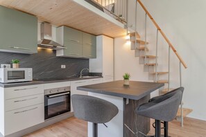 A modern kitchen with a central island, built-in oven, and a microwave. There is a staircase with wooden steps and a railing.