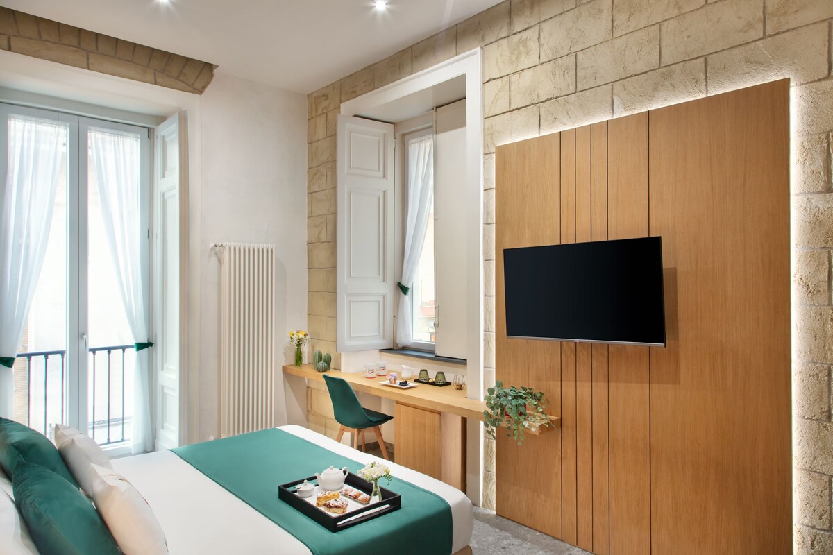 A modern hotel room with a bed, a desk, a TV, and a window with curtains.