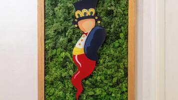 A framed artwork with a character wearing a crown and a red scarf, set against a green leafy background.