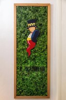 A framed artwork with a character wearing a crown and a red scarf, set against a green leafy background.