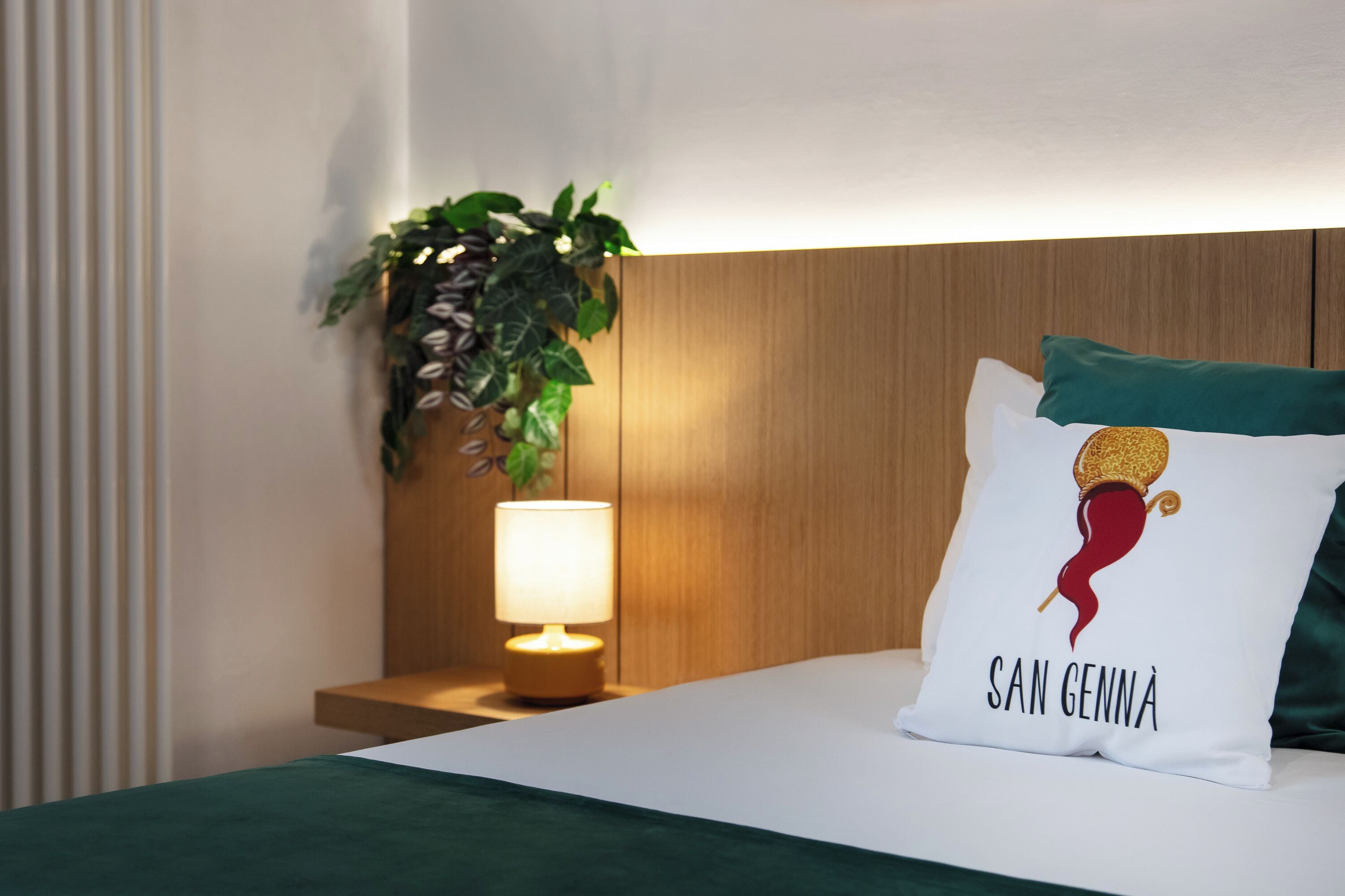 A neatly made bed with a pillow featuring a seahorse design and the text "SAN GENNA".