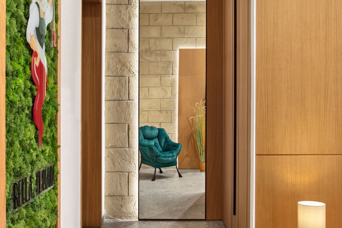 A hallway with a green wall, a teal chair, and a wooden bench with a lamp.
