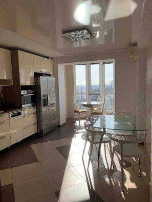 Une cuisine moderne dotée d’appareils électroménagers en acier inoxydable, d’une table à manger en verre et offrant une vue sur la ville grâce à de grandes fenêtres.