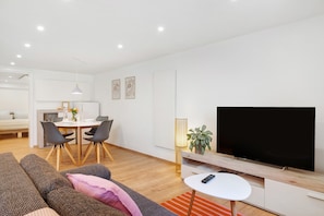 A modern living room with a flat-screen TV, a dining area with a table and chairs, and a cozy seating area with a sofa and a small white table.