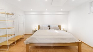 A bedroom with a wooden bed, white walls, a wooden floor, a bedside table with a lamp, and a metal shelf unit. - Apartment 'Apfelwiese' with Private Terrace, Garden, and Wi-Fi (Meßstetten)