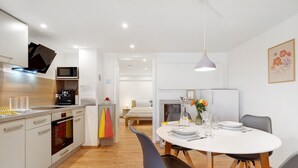 A modern kitchen with a microwave, oven, and sink. There is a dining area with a table, chairs, and a vase with flowers. - Apartment 'Apfelwiese' with Private Terrace, Garden, and Wi-Fi (Meßstetten)