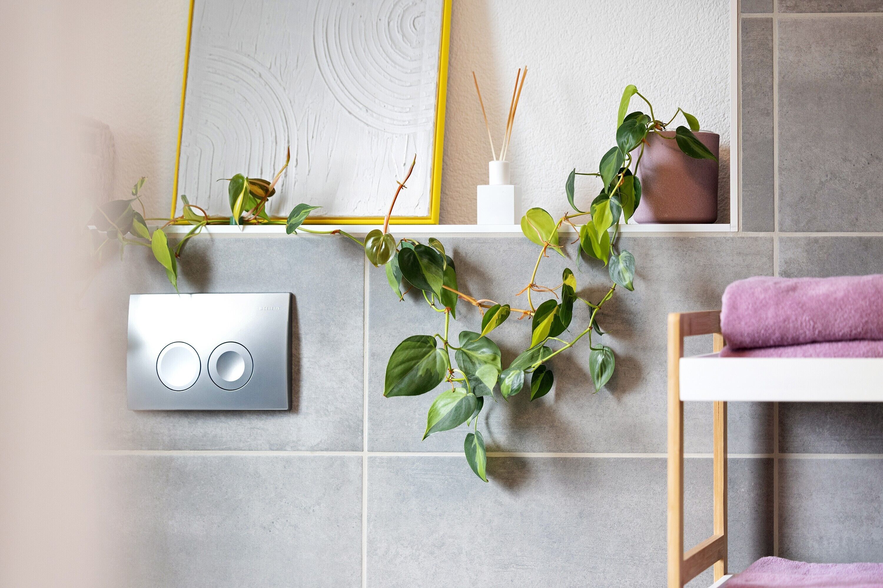 Bagno con termosifone a parete, un'opera d'arte incorniciata, una pianta in vaso e una sedia di legno con un asciugamano.