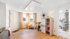 A modern living room with a sofa, a wooden coffee table, a small bench, a potted plant, a bookshelf, and a glass shower enclosure. - Apartment 'Apfelwiese' with Private Terrace, Garden, and Wi-Fi (Meßstetten)