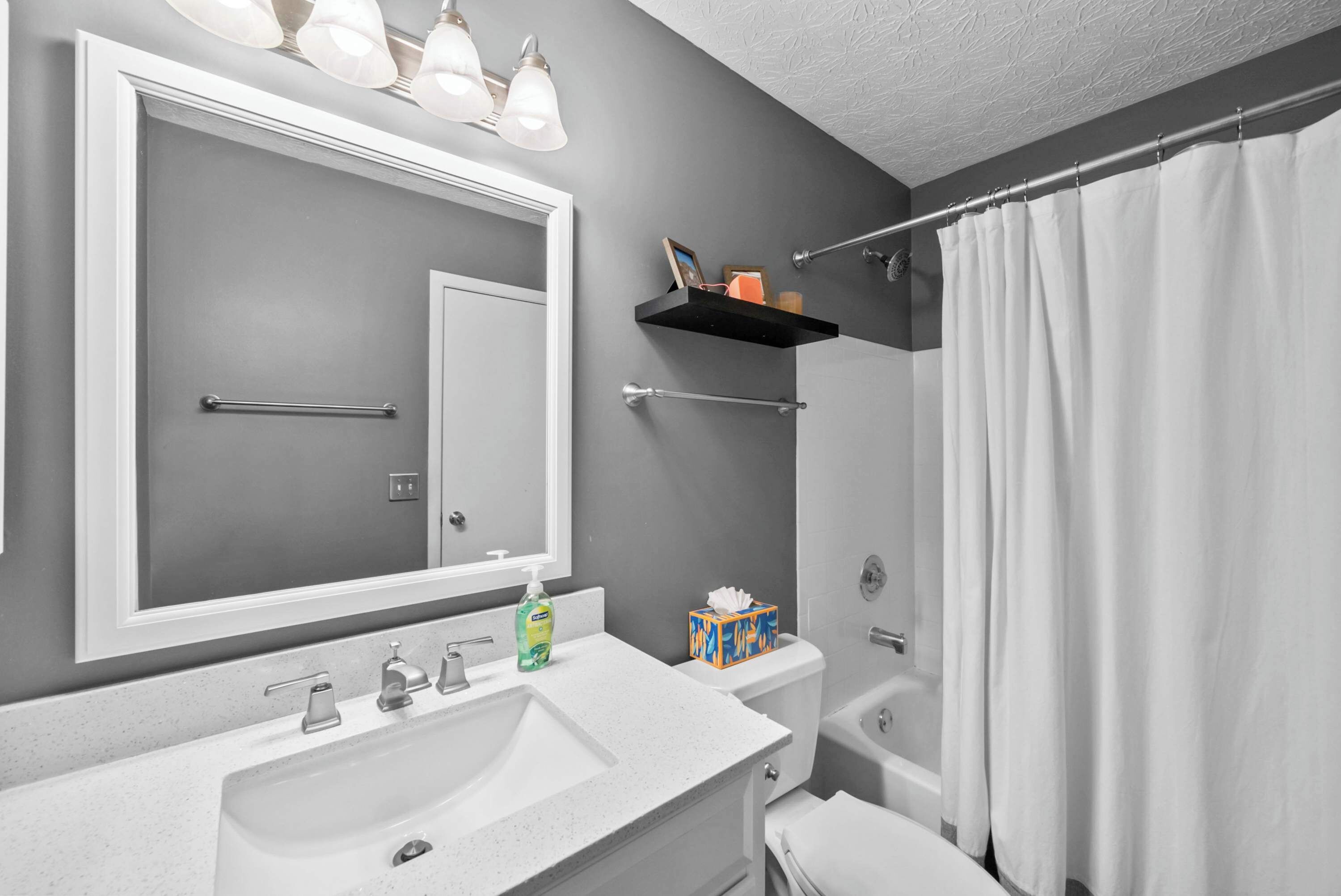 A bathroom with a large mirror, a sink, a toilet, and a shower curtain.
