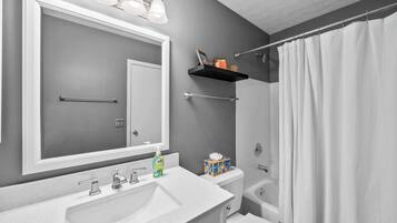 A bathroom with a large mirror, a sink, a toilet, and a shower curtain.