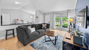 Un salón moderno con un sofá gris, una mesa de centro redonda y un televisor sobre un mueble de madera.
