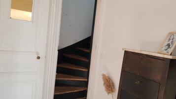 A white door with a small mirror, a wooden staircase, and a dark wooden dresser with a picture frame.