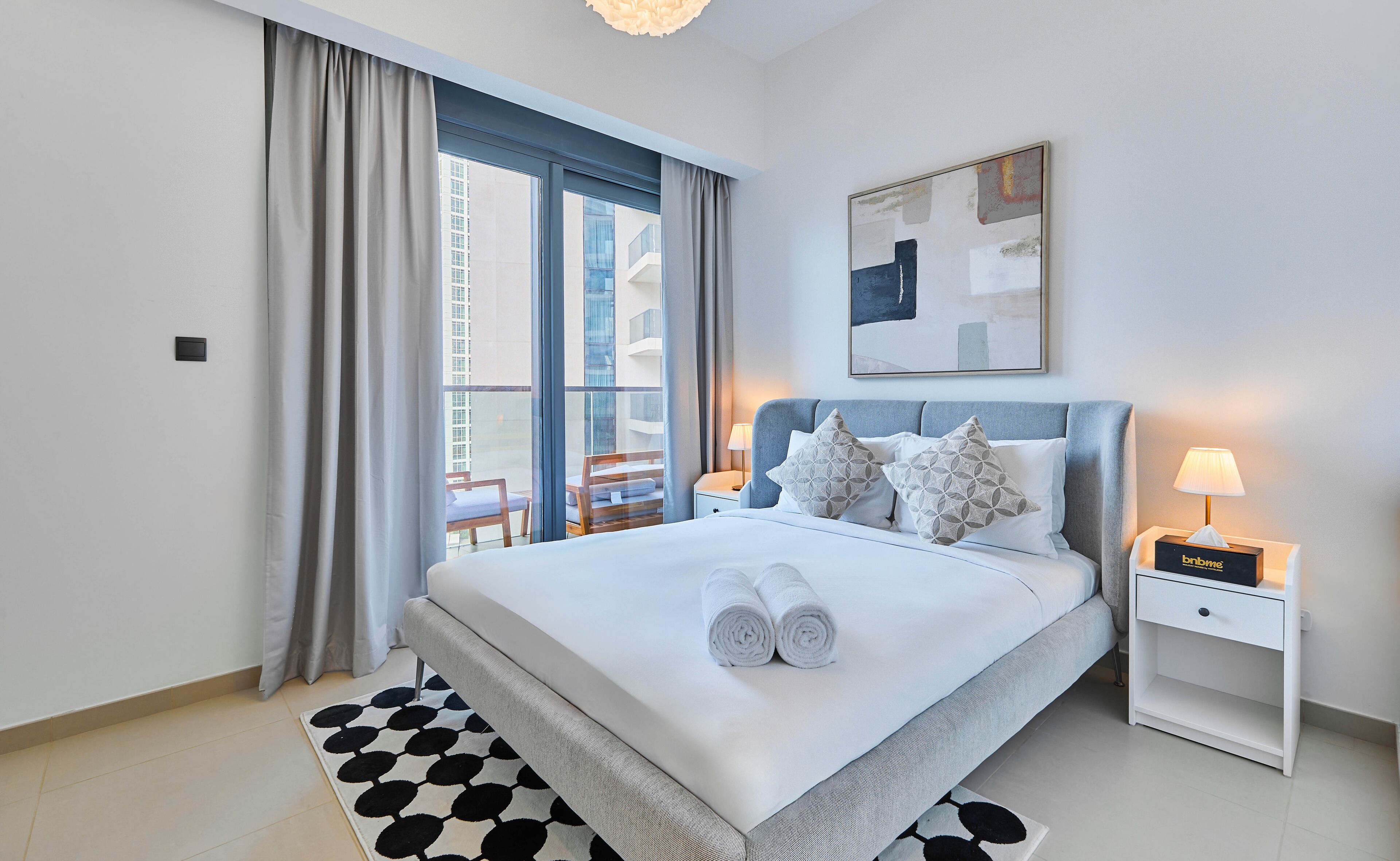 Habitación de hotel moderna con una cama grande, una mesita de noche, una lámpara y vistas de la ciudad desde la ventana.