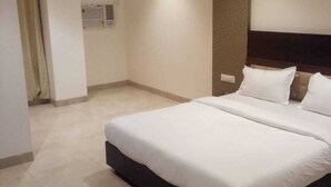 Ruime hotelkamer met een groot bed, een houten hoofdeinde en een neutraal kleurenschema.