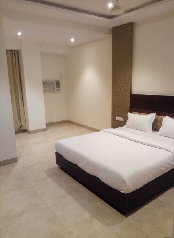 A spacious hotel room with a large bed, a wooden headboard, and a neutral color scheme.