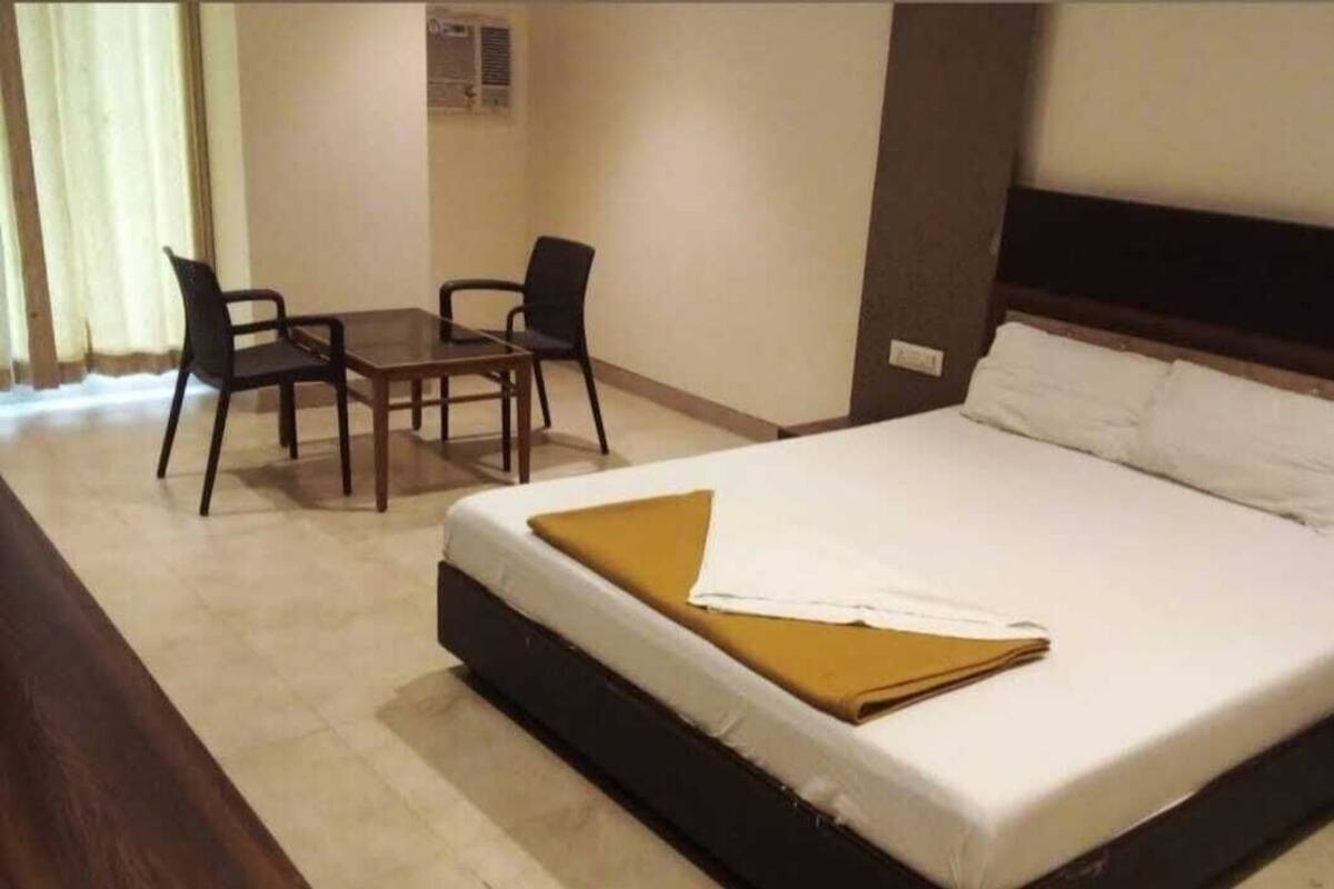 A hotel room with a bed, a desk, two chairs, and a window with curtains.