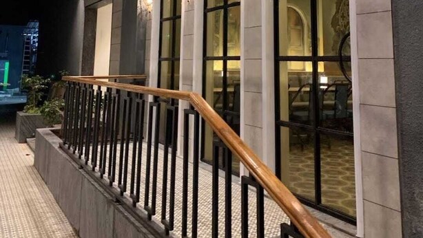 Een modern gebouw met een overdekt buitengebied, voorzien van een houten leuning en meerdere ramen met decoratieve verlichting.