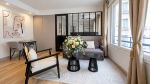 A modern living room with a sofa, two black side tables, a coffee table, a decorative vase, and a large mirror. - 1628 Matignon (Paris)