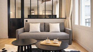 A modern living room with a grey sofa, two black round tables, and a cowhide rug. - 1628 Matignon (Paris)