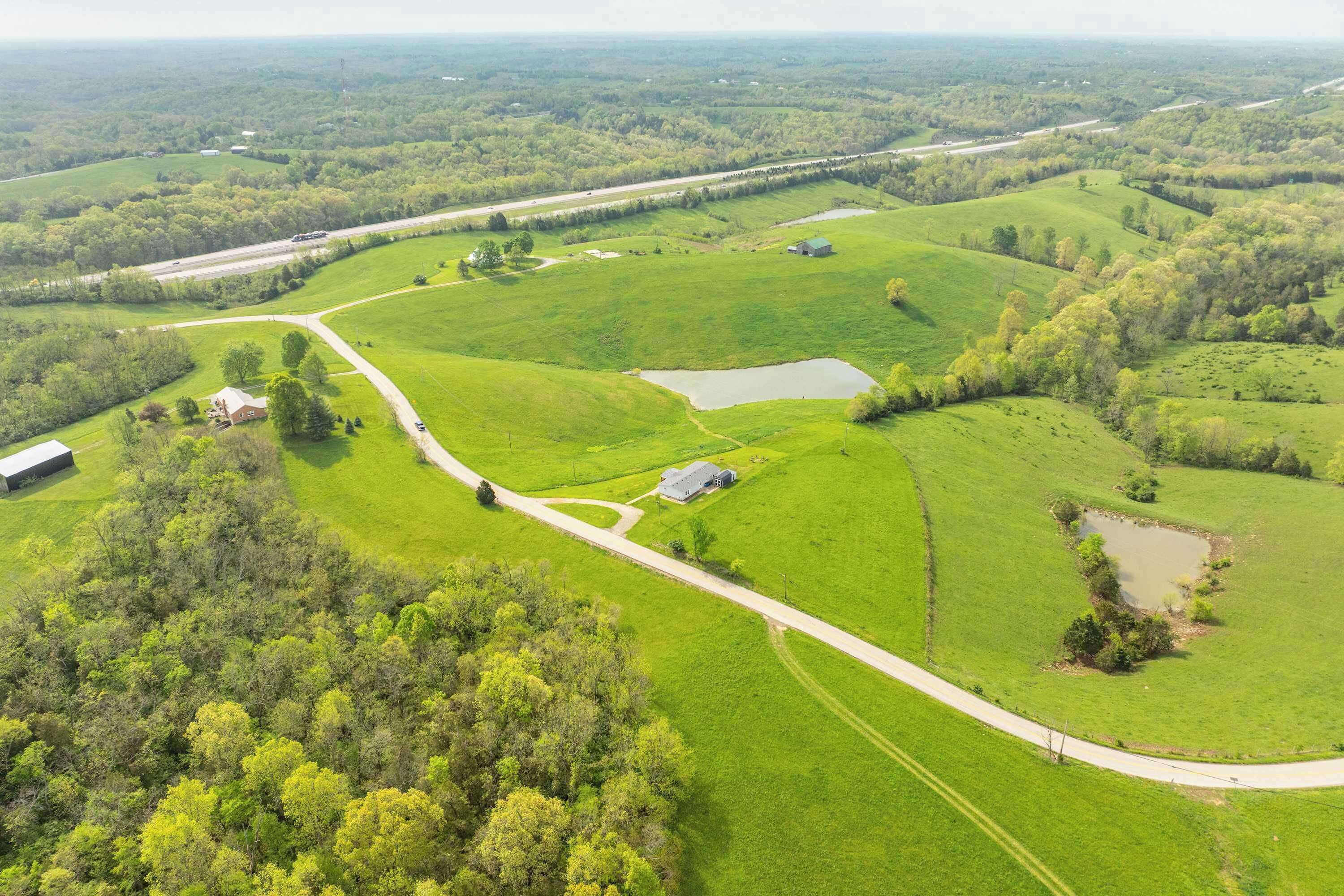 Vue aérienne d’un paysage rural avec des champs, une route et quelques bâtiments dispersés.