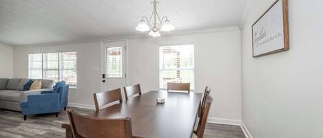A spacious dining area with a wooden table and chairs, a chandelier, and a framed inspirational quote on the wall.
