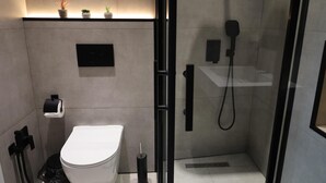 Un baño moderno con inodoro, ducha con mampara de vidrio y un pequeño estante con plantas en macetas.