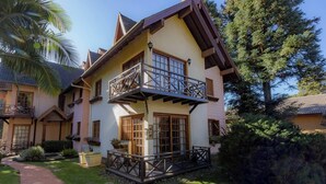 A two-story house with a balcony, a garden, and a pathway leading to the entrance. - Apartamento em Gramado próximo ao Parque Carrieri (Gramado)