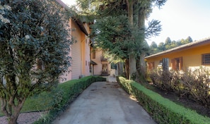 Un chemin menant à un bâtiment doté d’un balcon, entouré de verdure et d’arbres.