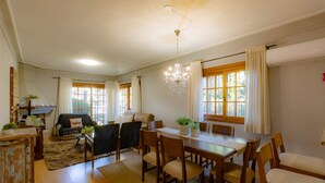 A spacious living room with a dining area, large windows with curtains, a chandelier, and a fireplace. - Apartamento em Gramado próximo ao Parque Carrieri (Gramado)