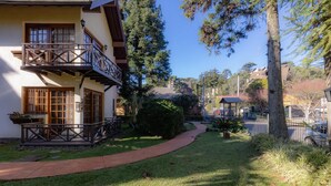 A two-story building with a balcony, a pathway leading to a gazebo, and surrounding greenery. - Apartamento em Gramado próximo ao Parque Carrieri (Gramado)