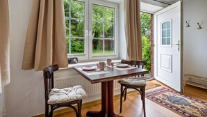 Ein Zimmer mit Tisch für zwei Personen, einem Heizkörper, einem Fenster mit Vorhängen und einer Tür.