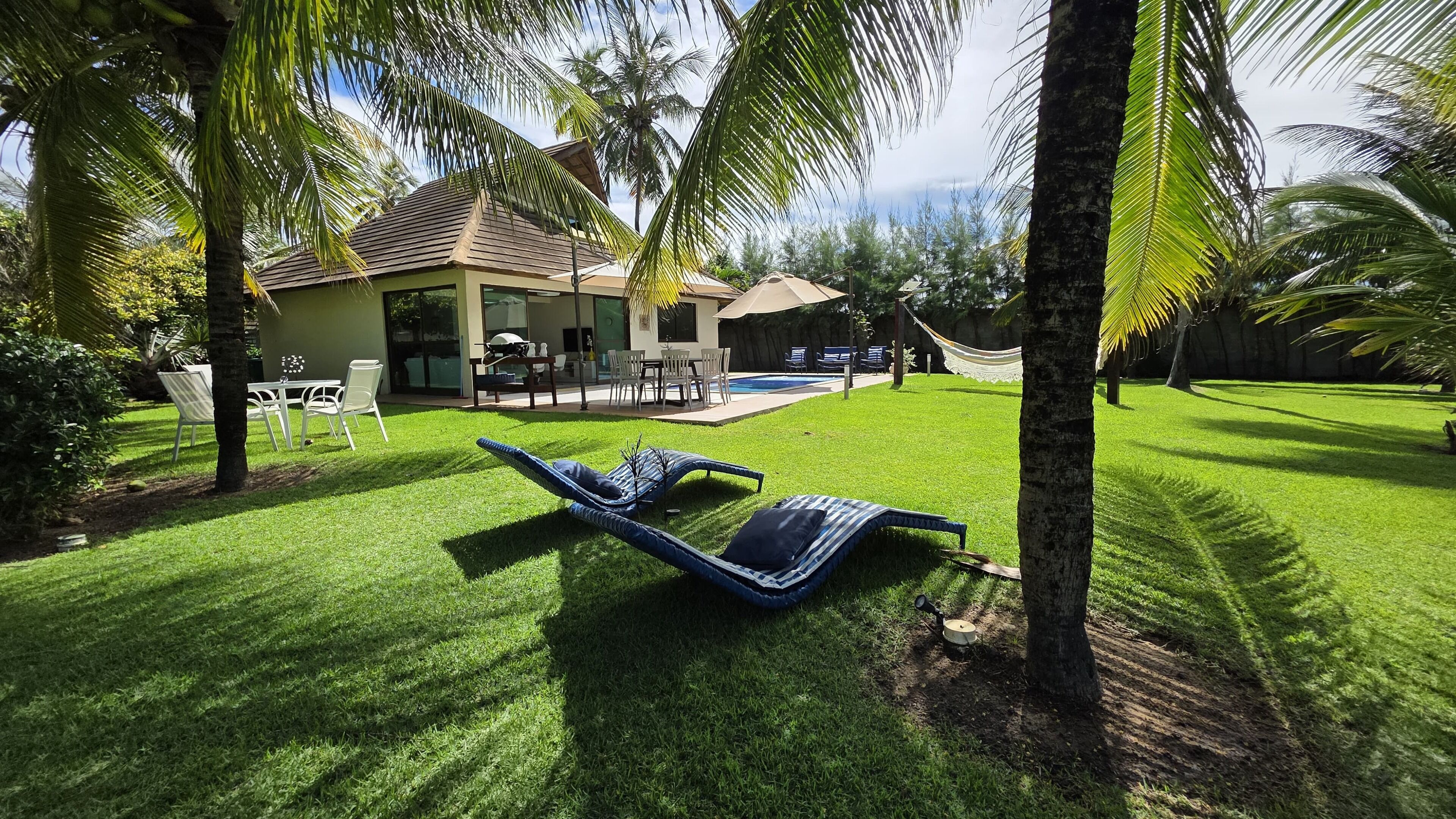 A backyard with a pool, lounge chairs, and a dining area.