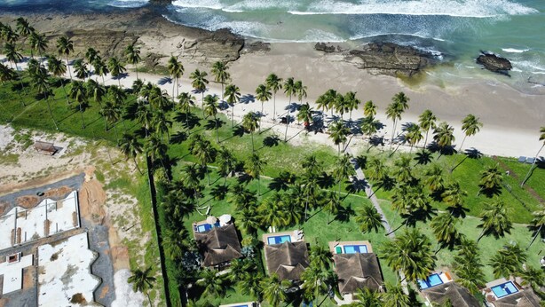 An aerial view of a beach resort with multiple bungalow-style accommodations, a sandy beach, and palm trees. - Bangalô Frente Mar no Carneiros Beach Resort bLP (Tamandaré)