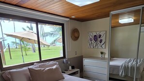 A bedroom with a large bed, a nightstand, a dresser, and a window with a view of greenery. - Bangalô Frente Mar no Carneiros Beach Resort bLP (Tamandaré)