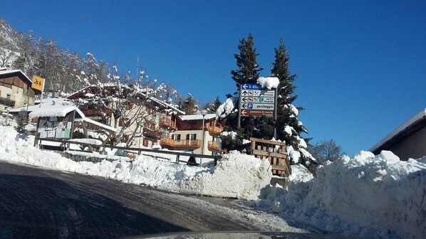 Un village de montagne enneigé, avec des bâtiments en bois, un panneau indicateur et un ciel bleu dégagé.