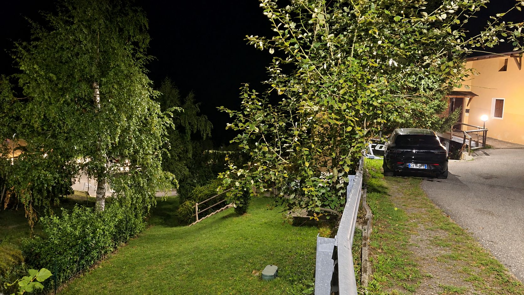 Vista nocturna d'una zona residencial amb una furgoneta aparcada, un jardí ben cuidat i una casa amb un porxo visible.