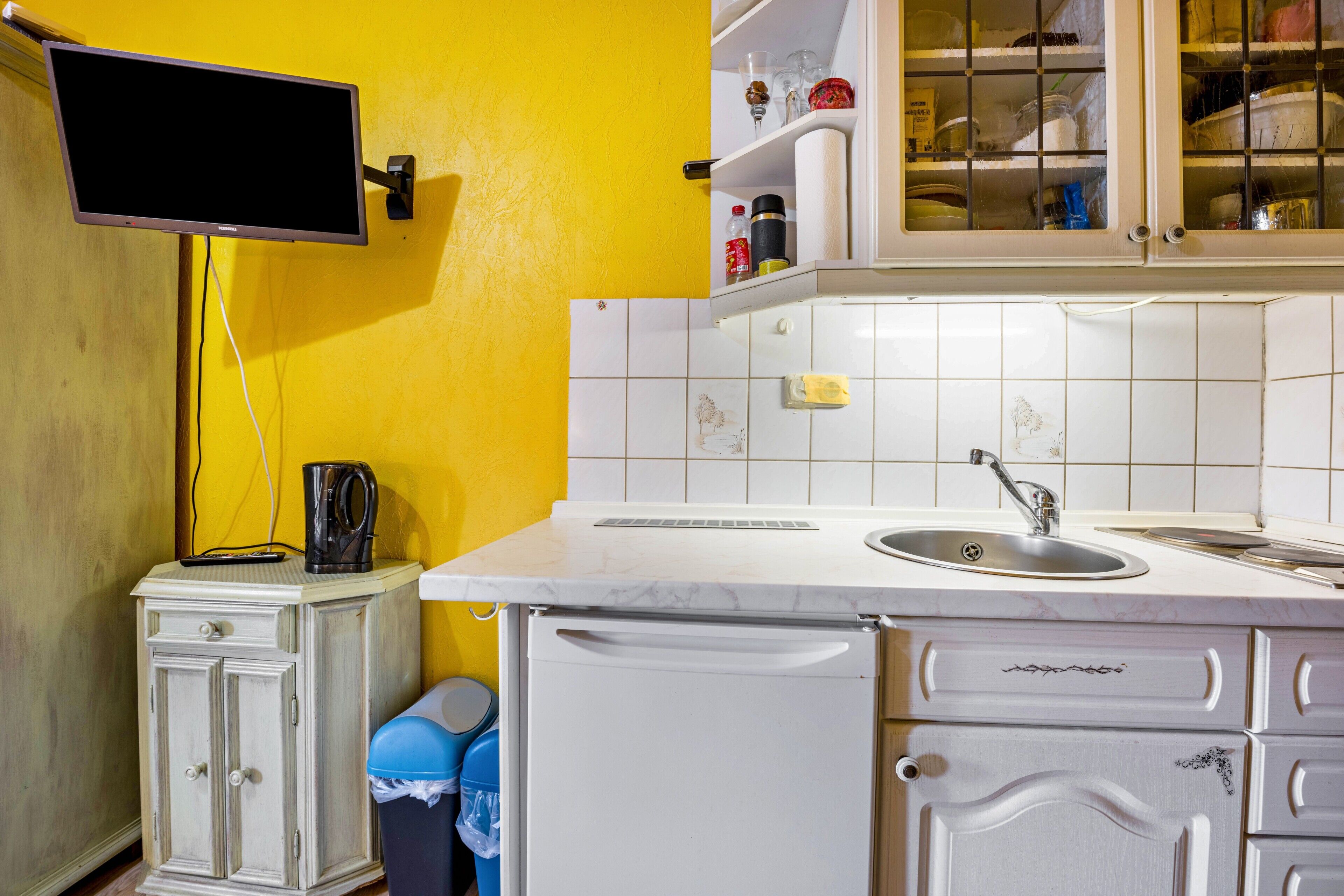 A kitchen with white cabinets, a sink, a countertop, and a television mounted on the wall.