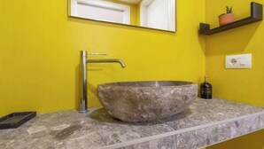 A bathroom with a large, round stone basin, a modern faucet, and a yellow wall. - House Brembo (Milano)