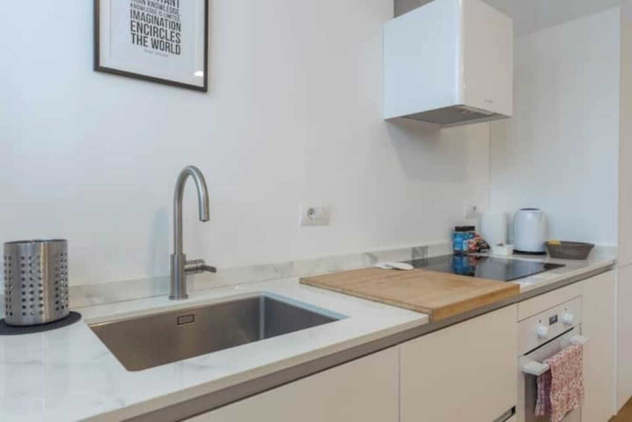 Una cocina moderna con un lavamanos de acero inoxidable, una tabla de cortar de madera y un armario blanco.