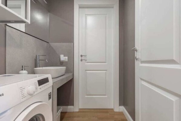 A compact bathroom with a washing machine, sink, and a white door. - Brembo House two (Milano)