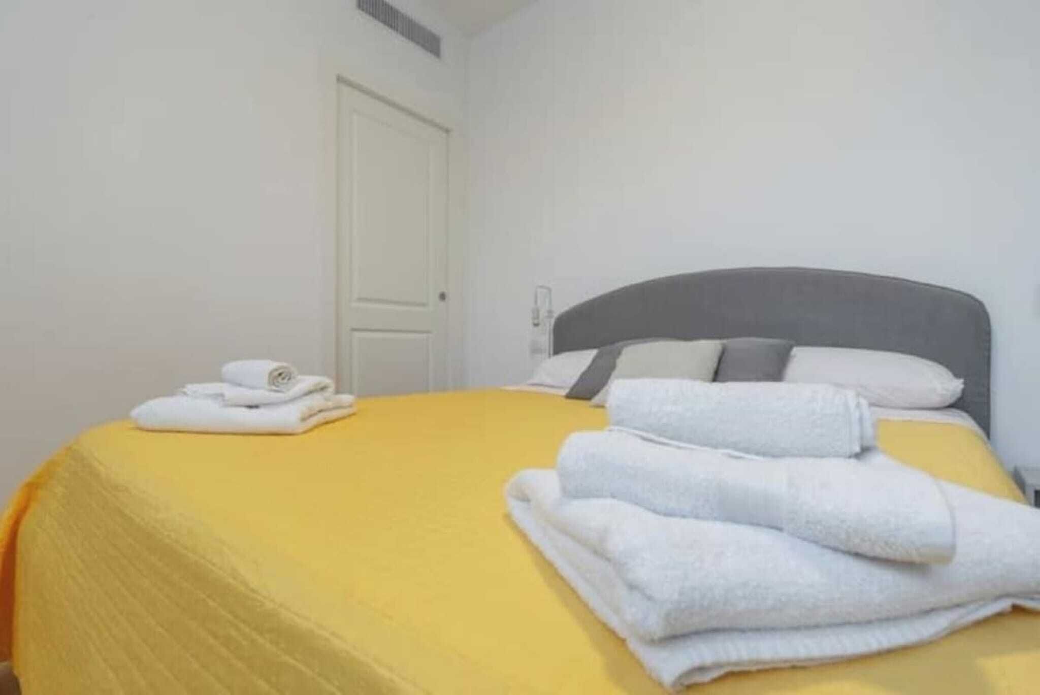 A hotel room with a bed covered in a yellow bedspread, white pillows, and folded towels.